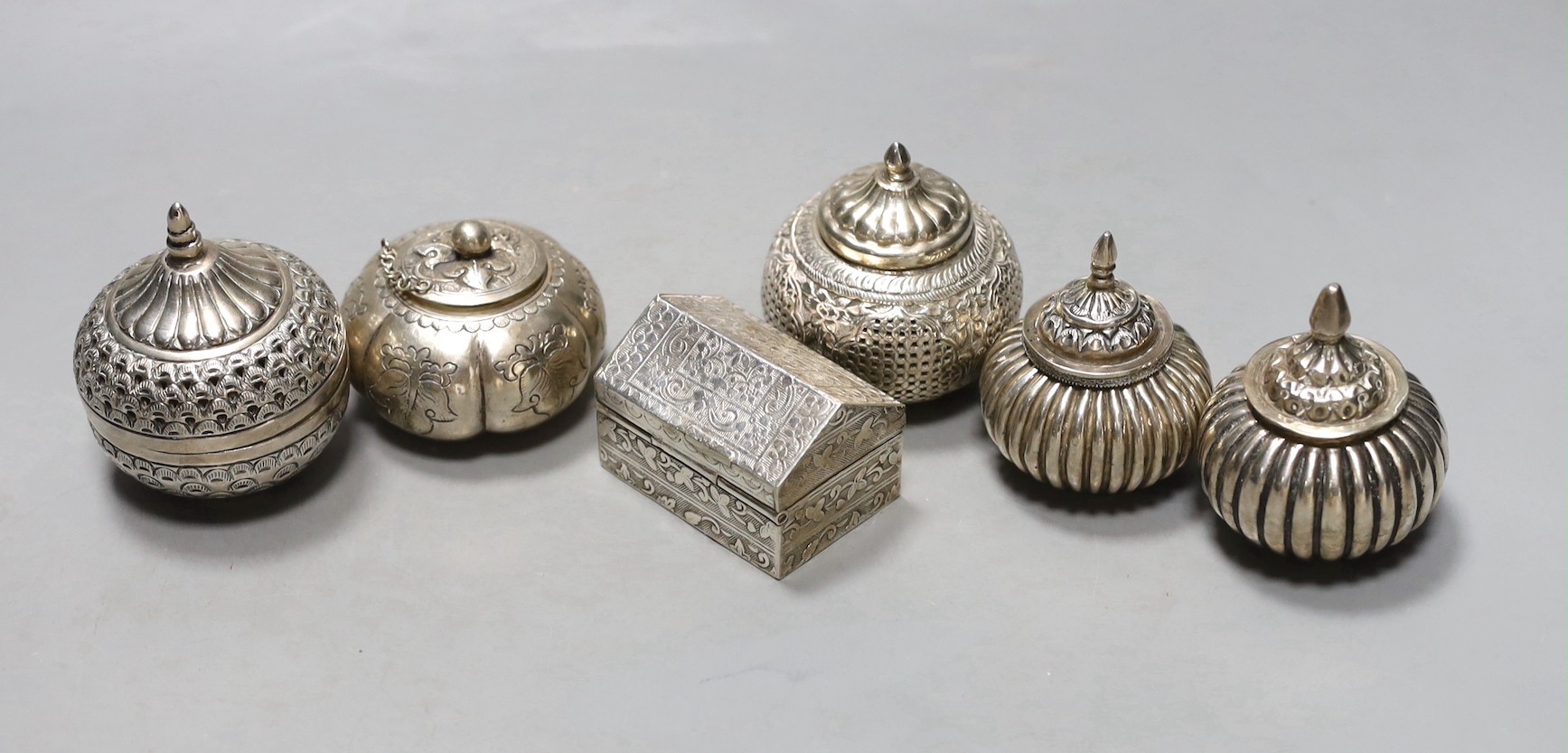 Five assorted 20th century Indian white metal circular boxes and covers including betel nut boxes and one other house shaped box and cover, largest diameter approx. 71mm.